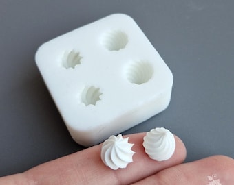Puede incluir: Un molde de silicona blanco con cuatro cavidades en forma de espiral. Dos pequeños objetos blancos en forma de espiral se sostienen en una mano. Los objetos parecen ser piezas decorativas en miniatura. El fondo es gris liso.