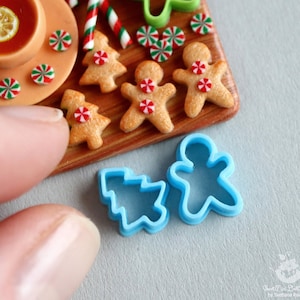 Può includere: Tagliabiscotti in plastica blu a forma di omino di pan di zenzero e albero di Natale. I tagliabiscotti sono su una superficie blu chiaro.