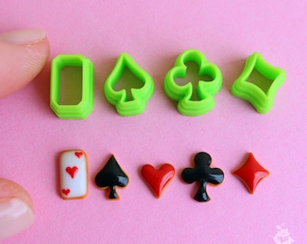 May include: Green plastic cookie cutters shaped like playing card suits: spades, clubs, diamonds, and hearts.  Also included are two red and white fondant cookies, one shaped like a playing card and the other shaped like a heart.