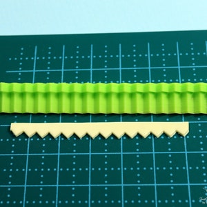 Może przedstawiać: Dwa silikonowe foremki do dekorowania ciast. G&oacute;rna foremka jest zielona i ma falisty brzeg. Dolna foremka jest beżowa i ma falisty brzeg.