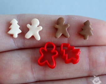 Op de afbeelding: Een close-up van zes miniatuur kerstkoekjesvormen. Twee zijn rode gingerbread men, twee zijn rode kerstboomvormen en twee zijn gemaakt van klei, een witte en een bruine.