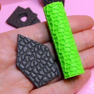 Puede incluir: Dos herramientas de decoraci&oacute;n de pasteles de silicona, una es un rodillo texturizado verde y la otra es una forma de diamante texturizada negra.