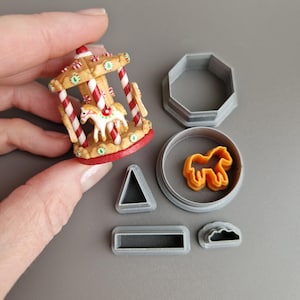 May include: A miniature carousel with a red base, white and red striped poles, and a horse figurine. Beside it are several grey plastic cookie cutters in various shapes, including a horse, octagon, triangle, rectangle, and a cloud.