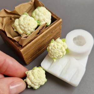 Pu&ograve; includere: Miniature di teste di cavolfiore in una cassa di legno con carta marrone. &Egrave; presente anche uno stampo in silicone bianco e una singola testa di cavolfiore. Il cavolfiore &egrave; bianco sporco con foglie verdi, ideale per progetti artigianali.