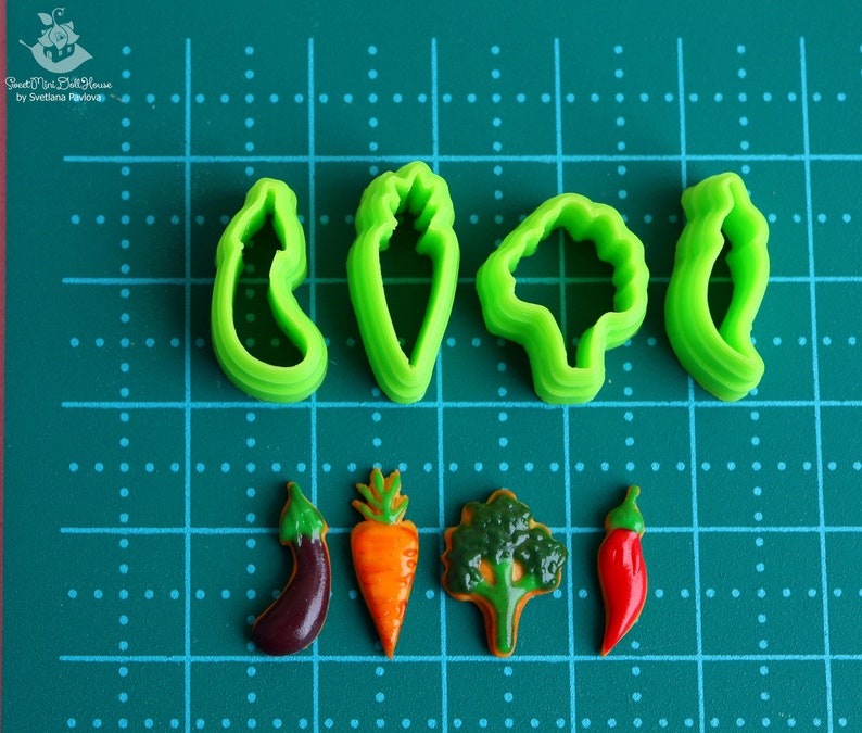 May include: Set of six green plastic cookie cutters shaped like vegetables, including a carrot, eggplant, pepper, broccoli, and two different types of leaves.  The cutters are arranged on a green cutting mat with white dots.
