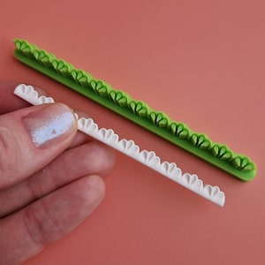 Op de afbeelding: Twee siliconen cakedecoratiegereedschappen, een groen en een wit, met een gegolfd randontwerp.