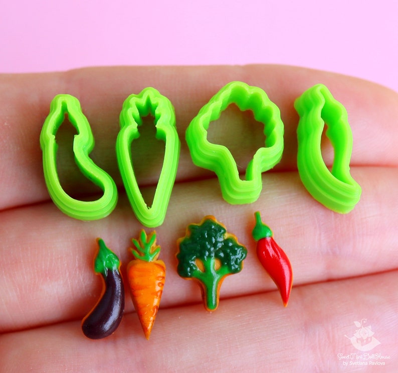 May include: A set of green plastic cookie cutters shaped like vegetables, including a carrot, broccoli, pepper, and eggplant. There are also miniature plastic vegetables, including a carrot, eggplant, broccoli, and a red chili pepper.