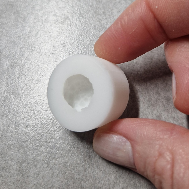 Pu&ograve; includere: Un oggetto cilindrico bianco con un centro cavo. L'oggetto &egrave; tenuto tra due dita. L'oggetto sembra essere fatto di un materiale liscio e solido. Lo sfondo &egrave; una superficie grigia strutturata.