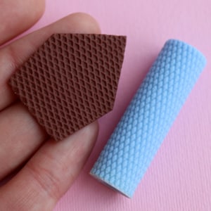 Puede incluir: Dos piezas de espuma texturizada, una marrón y otra azul claro. La pieza marrón tiene forma de casa y la pieza azul es un cilindro.
