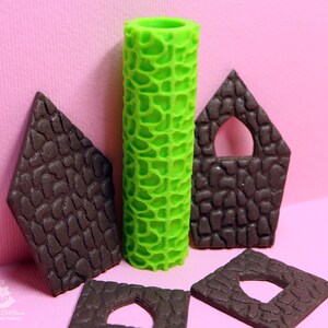 Puede incluir: Un conjunto de cinco herramientas para decorar pasteles, que incluyen un rodillo verde y cuatro piezas de fondant marr&oacute;n con ventanas recortadas. Las herramientas se utilizan para crear una textura de piedra en los pasteles.