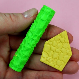 May include: Two green and yellow silicone cake decorating tools. One is a rolling pin with a brick pattern and the other is a brick-shaped mold.