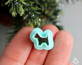May include: A light blue plastic cookie cutter shaped like a dog. The cookie cutter is held in a hand.