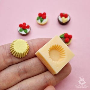 Puede incluir: Un molde de silicona amarillo para hacer pasteles o cupcakes en miniatura. El molde tiene forma de papel para cupcakes con un borde acanalado. También se muestran en la imagen varios cupcakes en miniatura hechos con el molde.