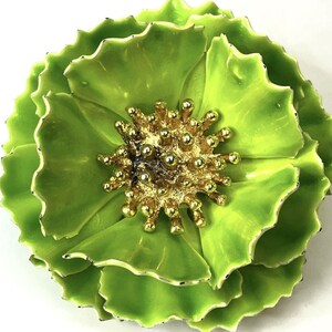 May include: A floral brooch featuring layered, lime green enamel petals with scalloped edges. The center of the flower is composed of a textured, gold-toned cluster of small, rounded stamens that contrast with the smooth, vibrant green petals.