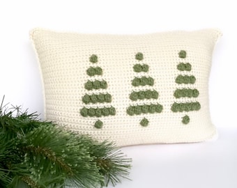 Puede incluir: Una almohada de crochet blanca con tres árboles de Navidad de crochet verde en la parte delantera.