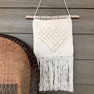 Peut inclure: Suspension murale en crochet blanc avec un motif en forme de cœur et des franges. La suspension est fixée à une branche de bois flotté.