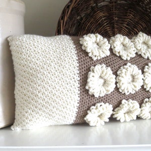 May include: A white and brown crocheted pillow with a textured design. The pillow has a white side with a simple stitch and a brown side with raised white flowers.
