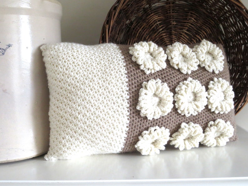 May include: A white and brown crocheted pillow with a textured design. The pillow has a white side with a simple stitch and a brown side with raised white flowers.