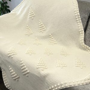 May include: A white crocheted throw blanket with a textured pattern of small white pom-poms arranged in a geometric design.