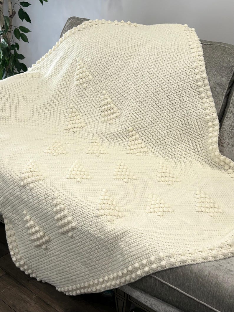 May include: A white crocheted throw blanket with a textured pattern of small white pom-poms arranged in a geometric design.