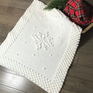 May include: White crocheted baby blanket with a snowflake design. The blanket has a textured border and is made with a soft yarn.