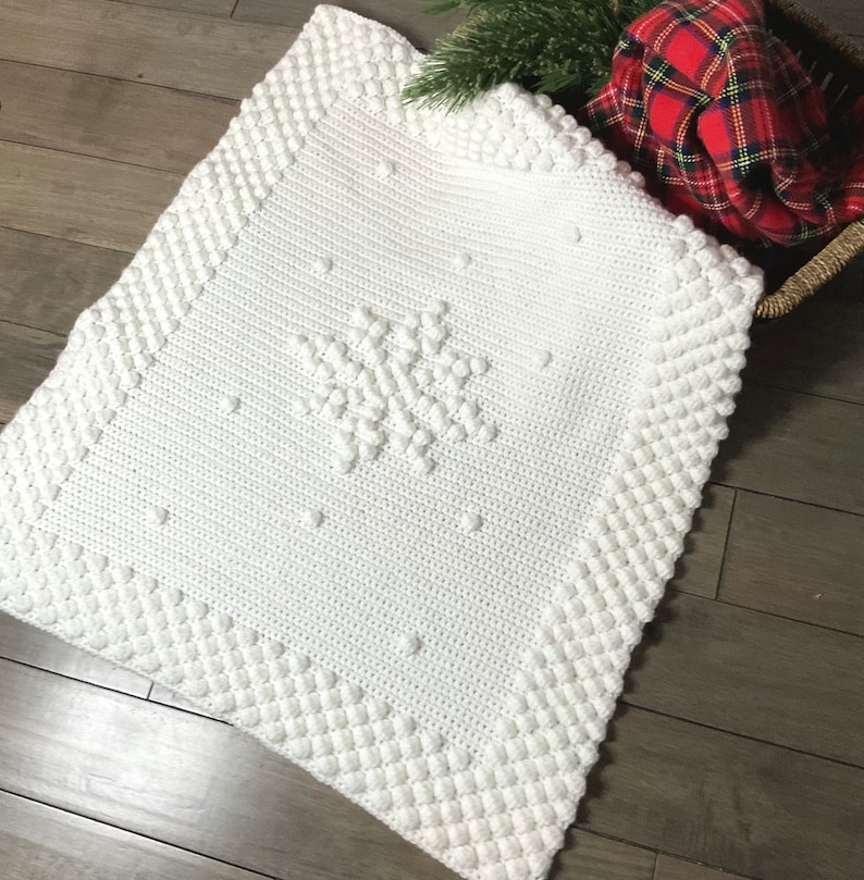 May include: White crocheted baby blanket with a snowflake design. The blanket has a textured border and is made with a soft yarn.