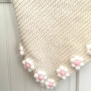 May include: A white crocheted baby blanket with a border of pink and white crocheted flowers.