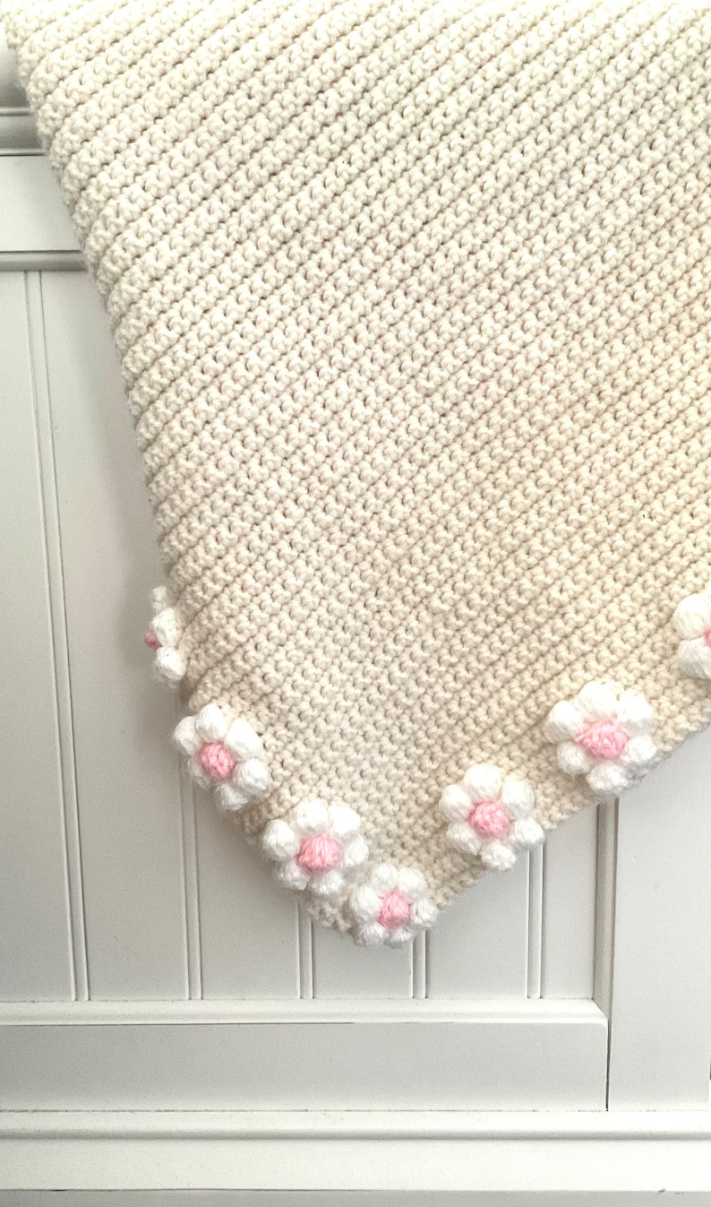 May include: A white crocheted baby blanket with a border of pink and white crocheted flowers.