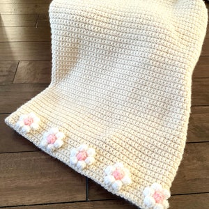 May include: A cream-colored crocheted blanket with a border of pink and white crocheted flowers.