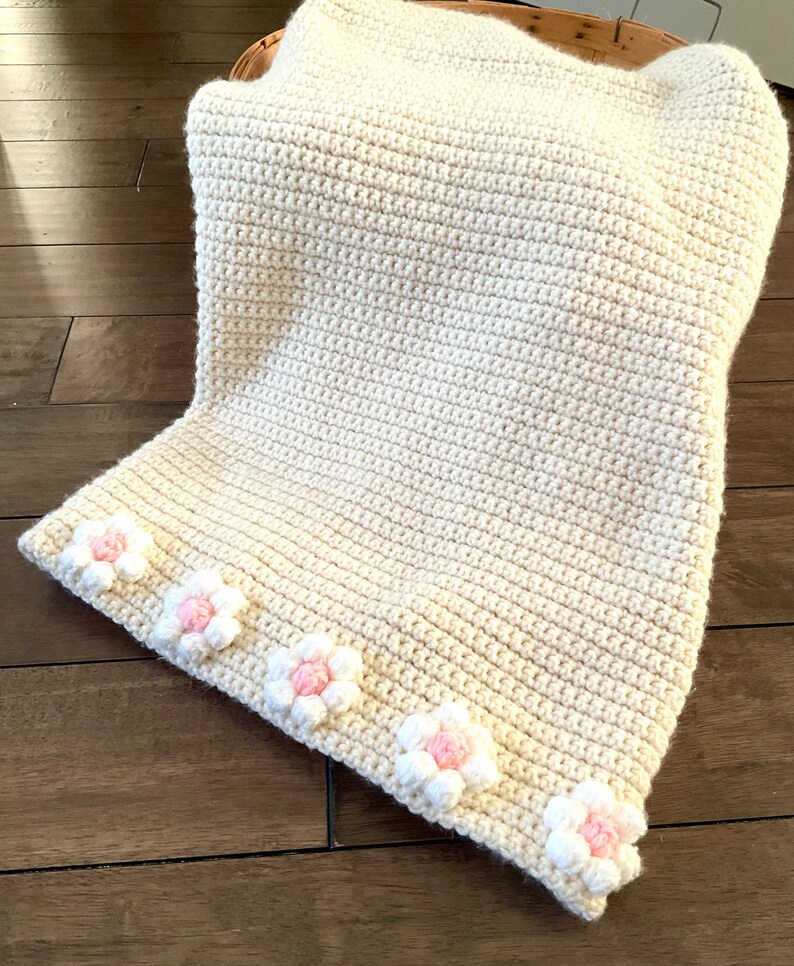 May include: A cream-colored crocheted blanket with a border of pink and white crocheted flowers.