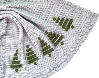 May include: A grey crocheted blanket with a green crocheted tree design. The blanket is folded in half and the edge is visible.