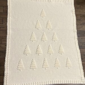 May include: A white crocheted blanket with a design of multiple white crocheted Christmas trees.