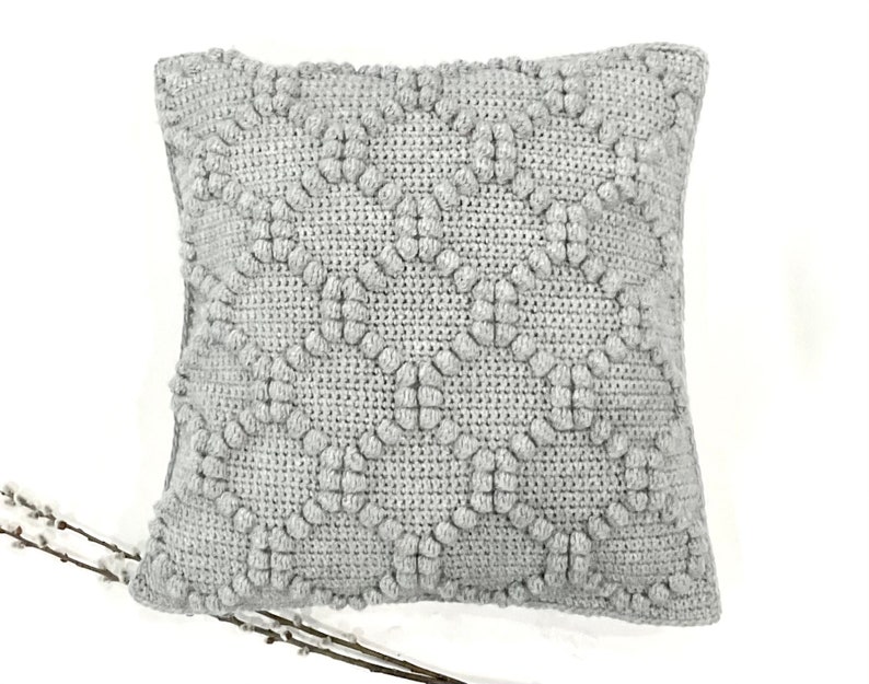 May include: A gray, textured, square pillow with a raised diamond pattern. The pillow is made of a soft, plush fabric.