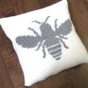 May include: White crocheted pillow with a gray crocheted bee design.