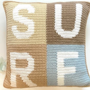 Könnte beinhalten: Ein gehäkeltes Kissen mit dem Wort "SURF" in weißer Wolle auf einem beige, braunen und hellblauen Hintergrund.