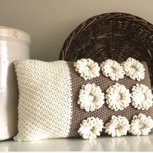 May include: A brown and white crocheted pillow with a textured design. The pillow has a brown background with white crocheted flowers.