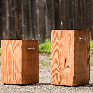 May include: Two wooden boxes with metal handles. The boxes are different sizes and are made of natural wood with a reddish-brown stain. The boxes are sitting on a gray surface.