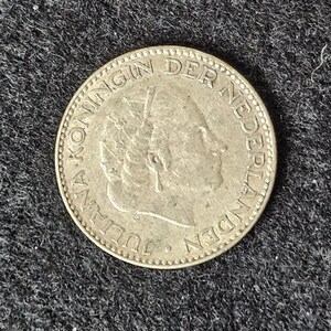 May include: Silver Dutch coin with the text "KONINGIN DER NEDERLANDEN JULIANA" around the edge and a portrait of Queen Juliana in the center.