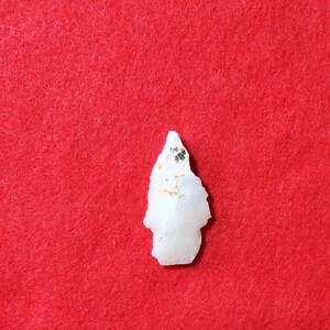 May include: A white arrowhead with brown and black flecks, on a red felt background.