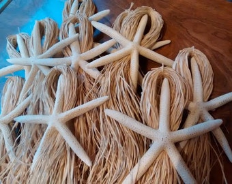 May include: Several white starfish with natural fiber accents are arranged on a wooden surface. The starfish have five arms and are a light, natural color. The fiber adds a rustic, beachy aesthetic.