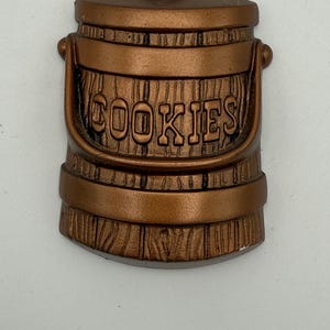 May include: A brown ceramic cookie jar shaped like a wooden bucket with the word "COOKIES" embossed on the front.