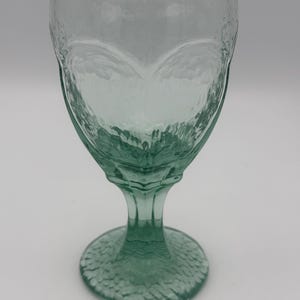 May include: A green glass goblet with a textured, embossed design. The goblet has a wide bowl and a tall stem with a round base.
