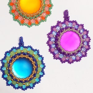 May include: Three beaded pendants with colorful glass cabochons in the center. The pendants are made with green, pink, and purple beads, and gold beads around the cabochons.