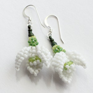 May include: A pair of silver earrings with white and green beaded snowdrop flowers.