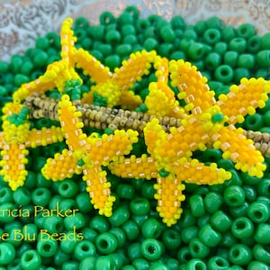 Könnte beinhalten: Nahaufnahme einer Perlenblume aus gelben und grünen Perlen. Die Blume ist von grünen Perlen umgeben. Der Text "Patricia Parker Rose Blu Beads" ist am unteren Rand des Bildes sichtbar.