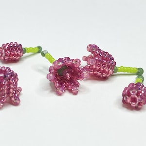 Può includere: Cinque ciondoli a forma di fiore in perle rosa con steli verdi. I fiori sono realizzati con piccole perle iridescenti e hanno un design delicato a forma di campana.