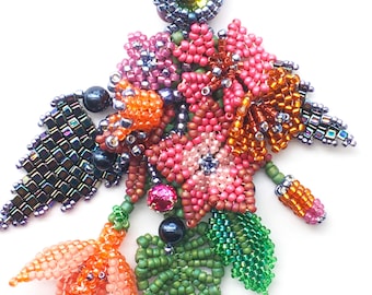 May include: A beaded flower brooch with a variety of colors, including pink, orange, green, and purple. The brooch features a central green gem and is made with iridescent beads.