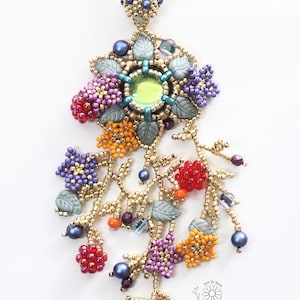 May include: A beaded necklace with a flower pendant featuring a green gemstone surrounded by colorful beads and leaves. The pendant hangs from a gold chain with multiple strands of beads and leaves. The necklace is made by Sunfish Pond.