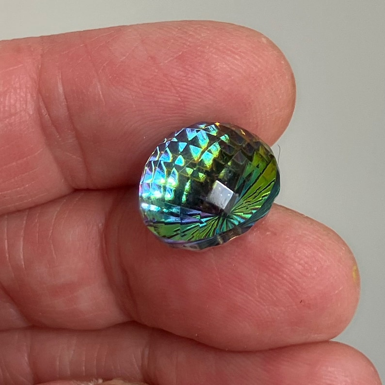 May include: A iridescent green and blue faceted glass bead with a diamond-shaped pattern.