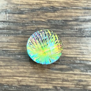 May include: A round iridescent glass bead with a swirling pattern of green, blue, and yellow.